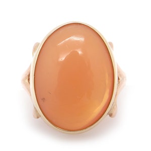 May include: A gold ring with an oval-shaped carnelian gemstone. The ring has a delicate design with intricate details.