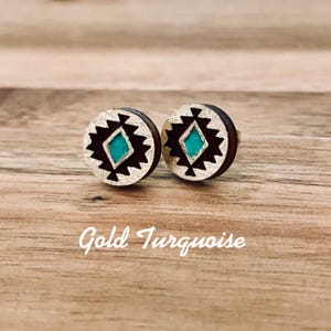 May include: A pair of small, round, wooden earrings with a geometric design in black, silver, and turquoise. The earrings feature a diamond shape in the center with a turquoise inlay.