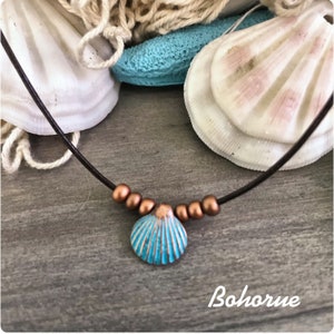 May include: A turquoise seashell pendant necklace with copper beads on a brown leather cord. The necklace is displayed on a wooden surface with seashells in the background.