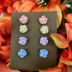 Può includere: Sei paia di orecchini a perno a forma di fiore su una carta marrone. Gli orecchini sono in tonalità di rosa, giallo, viola e blu.