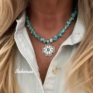 May include: A turquoise stone necklace with a silver pendant in a cross design. The necklace is made of small, irregular turquoise stones. The pendant has an oval turquoise stone in the center. The word "Bohorne" is written in the bottom left corner.