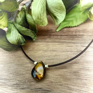 May include: A brown leather cord necklace with a teardrop-shaped tiger's eye gemstone pendant.