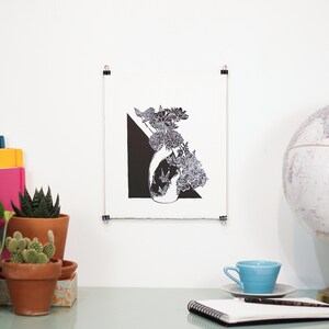 Bold black and white original linoleum block print of floral still life bouquet in a patterned vase hung with clips on a wall to show scale.