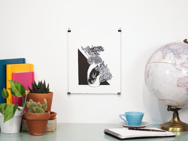 Bold black and white original linoleum block print of floral still life bouquet in a patterned vase hung with clips on a wall to show scale.
