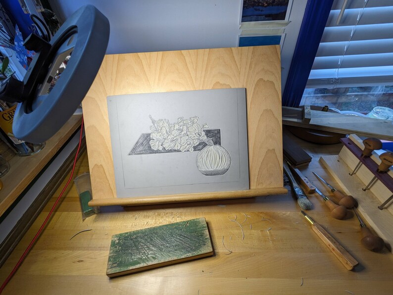 Linoleum block on artist work desk with carving and honing tools to show process.