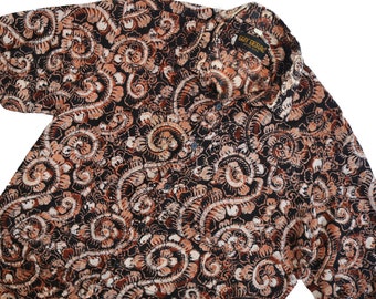 May include: A brown and black patterned button-up shirt with a paisley design. The shirt has a collar and a button closure. The label on the shirt reads "Gary Bertrand, Made in India."
