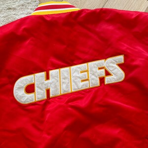 May include: Red satin bomber jacket with a white and yellow striped collar and the word "CHIEFS" embroidered in white with a yellow outline on the back.