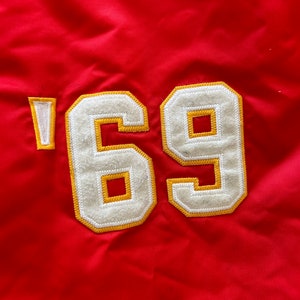 May include: Red fabric with a white and yellow embroidered patch that says '69'.