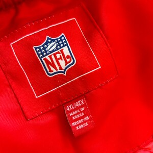 May include: A red NFL jacket with a white NFL logo and a red tag that says "4XL/4EX Made in Korea Hecho en Korea".