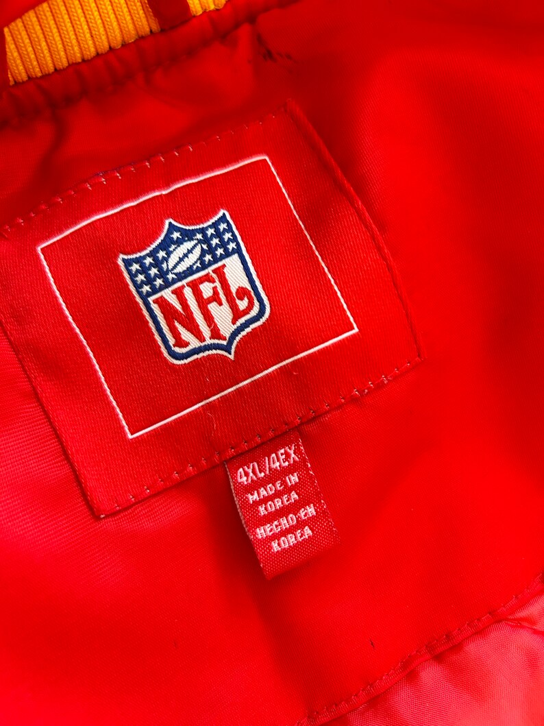 May include: A red NFL jacket with a white NFL logo and a red tag that says "4XL/4EX Made in Korea Hecho en Korea".