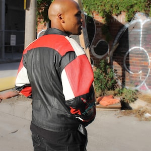 May include: A black leather jacket with red, white, and black panels. The jacket has a zipper closure and a stand-up collar.