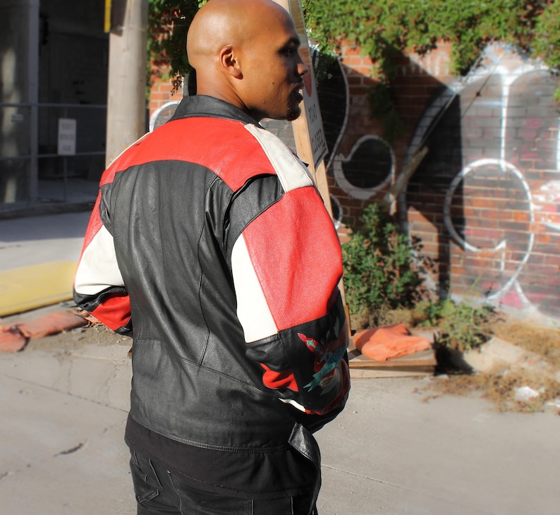 May include: A black leather jacket with red, white, and black panels. The jacket has a zipper closure and a stand-up collar.