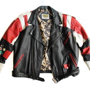 May include: A black leather motorcycle jacket with red and white panels. The jacket has a floral design on one sleeve and a zipper closure. The jacket has a brand label that says "Genuine Leather".