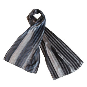 May include: A striped scarf in shades of gray and silver. The scarf is made of a silky material and has a subtle sheen.