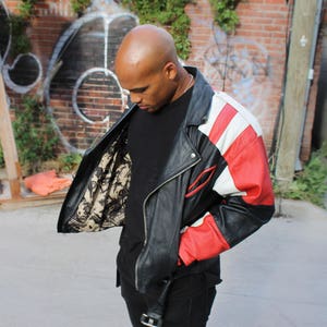 May include: A black leather jacket with red and white panels. The jacket has a zipper closure and a stand-up collar.