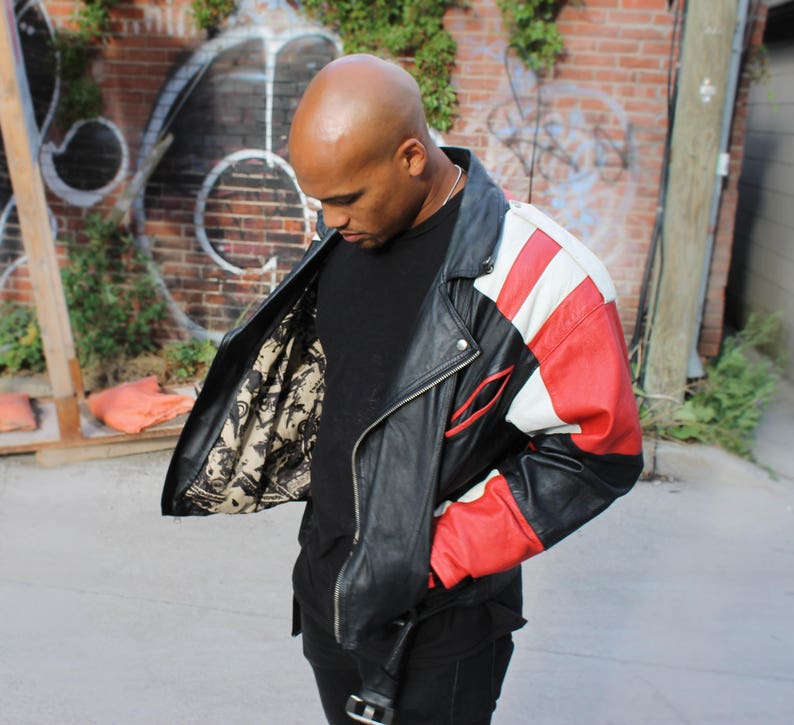 May include: A black leather jacket with red and white panels. The jacket has a zipper closure and a stand-up collar.