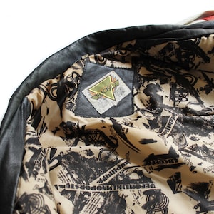 May include: Black leather jacket with a white and black patterned lining. The lining features a small black label with the text "Picket" in white.