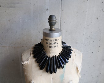 Peut inclure: Un collier ras de cou noir en forme de pointes angulaires. Le collier est présenté sur un mannequin avec le texte "MODERN MODEL FORMS" sur la poitrine.