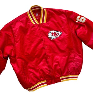 May include: Red satin bomber jacket with a white and yellow striped collar and cuffs. The jacket has a white embroidered logo of a Native American arrowhead with the letters "KC" inside. The number "6" is embroidered on the right sleeve.