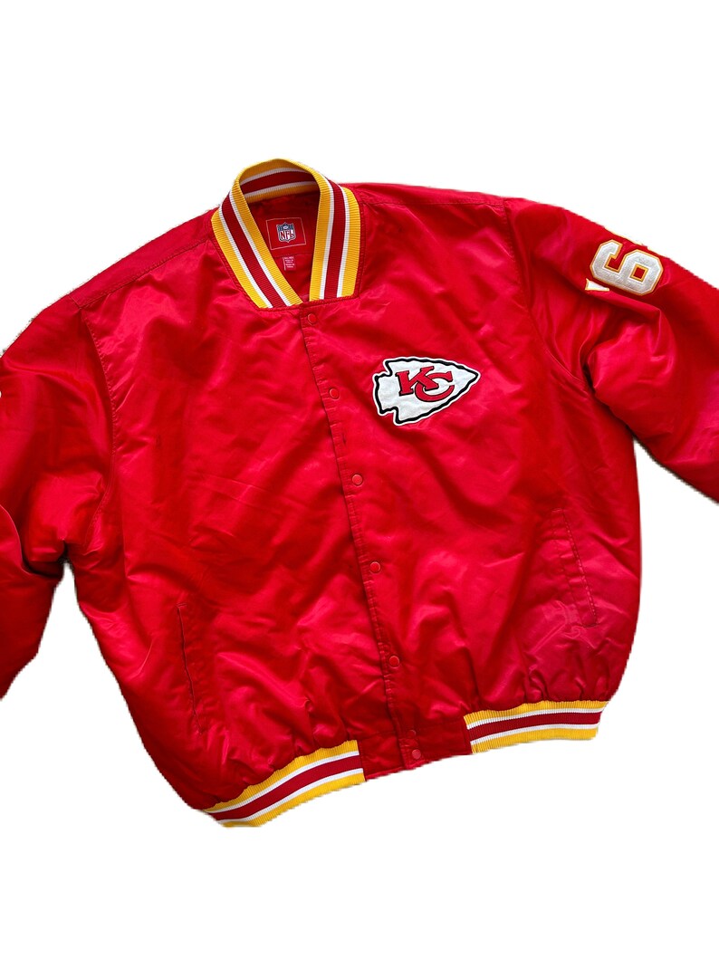 May include: Red satin bomber jacket with a white and yellow striped collar and cuffs. The jacket has a white embroidered logo of a Native American arrowhead with the letters "KC" inside. The number "6" is embroidered on the right sleeve.