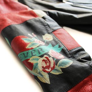 May include: A black leather jacket with red and white panels. The jacket has a floral design with the word "EVER" on the sleeve.