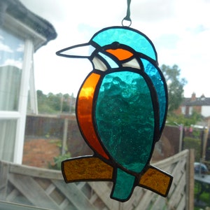 May include: A stained glass window hanging ornament depicting a blue and orange kingfisher bird with a brown branch.