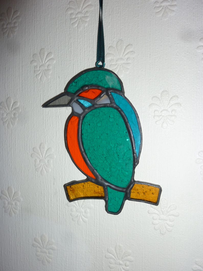 May include: A stained glass ornament of a kingfisher perched on a branch. The bird is green, blue, orange, and white.
