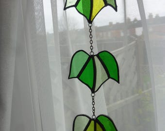 May include: A stained glass window hanging with three green, yellow, and white leaves connected by a silver chain.