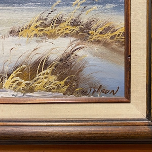 Op de afbeelding: Een close-up van een schilderij dat een besneeuwd landschap met hoog gras en een blauwe lucht afbeeldt. Het schilderij is rechtsonder getekend met "J. Wilson".