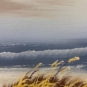 Op de afbeelding: Een schilderij van een zeegezicht met hoog gras op de voorgrond. De lucht is lichtblauw en het water is donkerblauw. Het gras is lichtbruin en geel.
