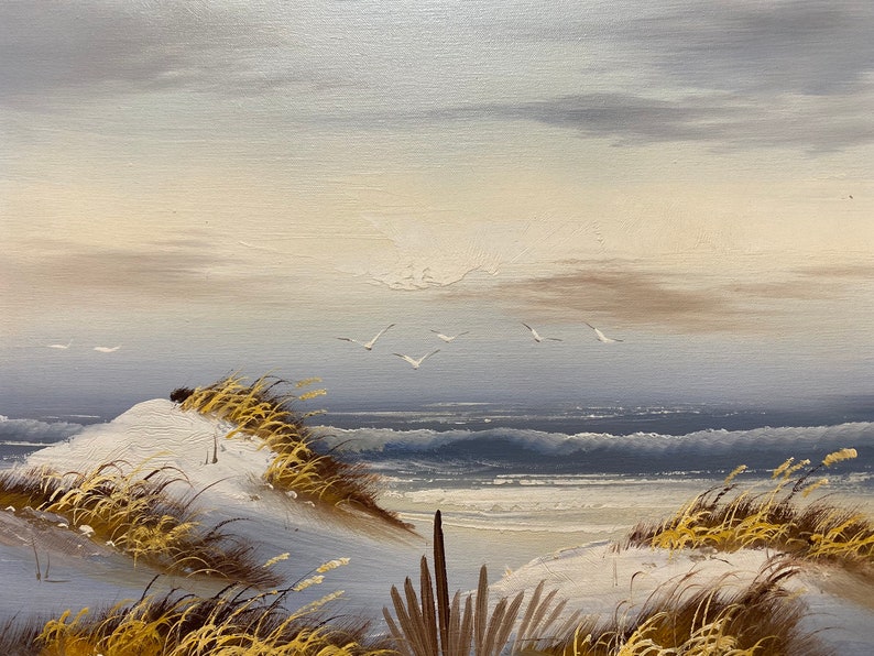 Op de afbeelding: Een schilderij van een zeelandschap met witte zandduinen, hoog gras en een blauwe zee met witte toppen. De lucht is lichtblauw met witte wolken.