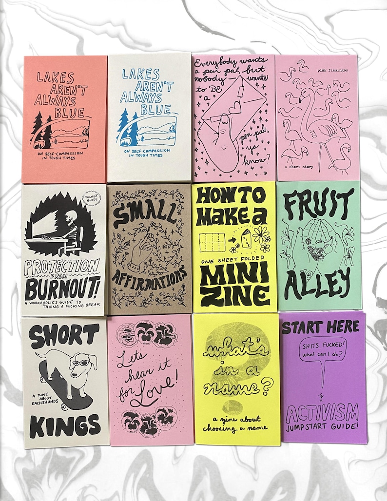 May include: A collection of twelve rectangular paper zines arranged in a grid, featuring various hand-drawn illustrations and text in black ink on colorful paper backgrounds including pink, cream, tan, yellow, green, and purple covers.