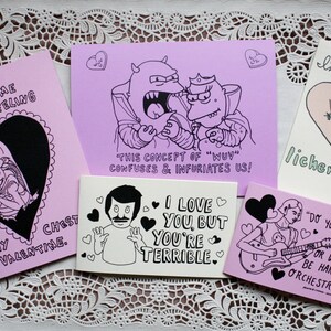 May include: A set of ten pink greeting cards with black and white illustrations and text. The cards feature various humorous messages about love and relationships. The text on the cards includes phrases like "You give me a funny feeling", "I love you, but you're terrible", and "This concept of 'wuv' confuses & infuriates us!"