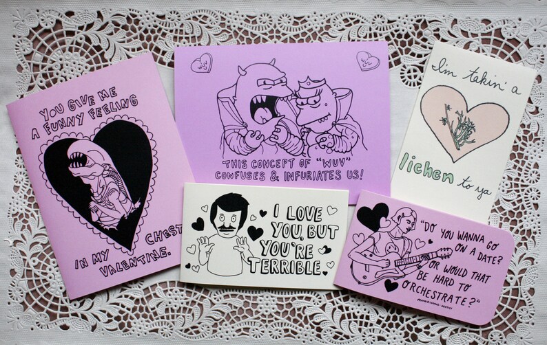 May include: A set of ten pink greeting cards with black and white illustrations and text. The cards feature various humorous messages about love and relationships. The text on the cards includes phrases like "You give me a funny feeling", "I love you, but you're terrible", and "This concept of 'wuv' confuses & infuriates us!"
