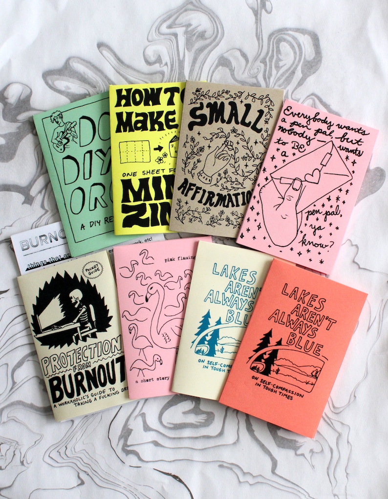 May include: A collection of eight small zines with various cover colors including light green, yellow, tan, pink, cream, and coral. Each booklet features unique black ink illustrations and hand-lettered text such as Protection From Burnout, Small Affirmations, and Lakes Aren't Always Blue, showcasing diverse graphic designs and themes.