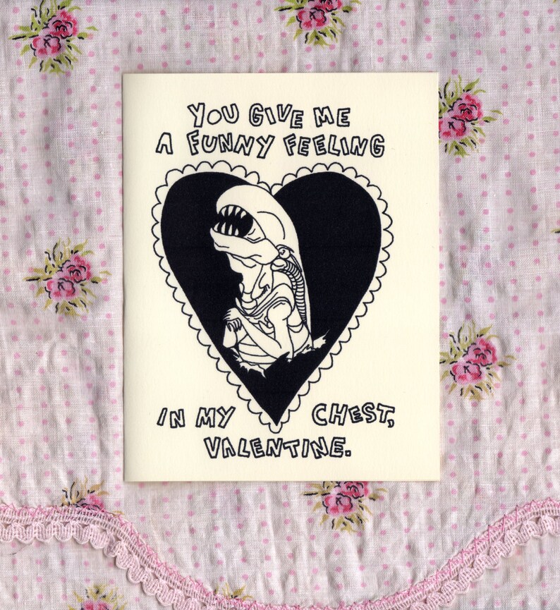 May include: A Valentine's Day card with a black and white illustration of an alien inside a heart. The card reads "You give me a funny feeling in my chest, Valentine."