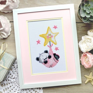 K&ouml;nnte beinhalten: Ein gerahmtes Kreuzstich-Design mit einem Pandab&auml;ren, der an einem gelben Stern mit einem Bienen Gesicht festh&auml;lt. Der Stern ist von rosa Sternen umgeben und der Panda tr&auml;gt ein rosa-wei&szlig; gestreiftes Outfit.