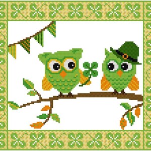 May include: Two green owls with yellow accents sit on a branch with green leaves. One owl is wearing a green hat with a gold band. The owls are surrounded by a green and yellow border with shamrock designs.