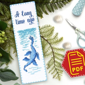 May include: A blue and white cross-stitch bookmark with a blue sea monster and the text "A long time ago".