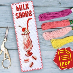 Puede incluir: Un marcapáginas de punto de cruz blanco con un diseño de batido de leche rojo y blanco. El marcapáginas tiene las palabras "MILK SHAKE" bordadas en hilo rojo. El marcapáginas está rodeado de hilo de bordar rosa, rojo, amarillo y blanco.