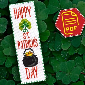 May include: A white cross-stitch bookmark with the text "Happy St. Patrick's Day" in red and green. The bookmark features a green shamrock and a black pot of gold.