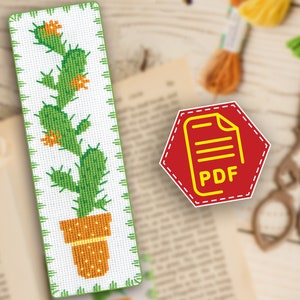 Pode incluir: Um padrão de ponto cruz para um marcador de página com um cacto verde em um vaso marrom com flores laranja. O padrão está em formato PDF.