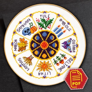 May include: A white circular cross-stitch pattern with a yellow, orange, and purple flower in the centre. The flower is surrounded by eight sections, each with a different symbol and name of a pagan holiday: Yule, Imbolc, Ostara, Beltane, Litha, Lammas, Mabon, and Samhain.