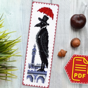 May include: Cross stitch pattern featuring a black crow wearing a top hat and holding a red umbrella, standing on a building with a clock tower. The pattern is on white fabric with red and white stitching around the edges.