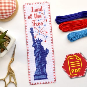 Könnte beinhalten: Ein Kreuzstich-Lesezeichen mit der Freiheitsstatue, Feuerwerk und dem Text "Land of the Free". Das Lesezeichen ist weiß mit blauen und roten Akzenten. Das Lesezeichen ist ein PDF-Download.