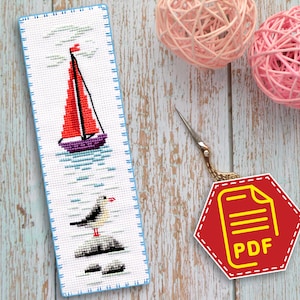 Può includere: Un segnalibro a punto croce con una barca a vela rossa con scafo viola, un gabbiano bianco appollaiato su rocce e onde blu. Il segnalibro è su uno sfondo di legno blu chiaro con un esagono rosso con un'icona PDF gialla e la parola "PDF" in testo giallo.