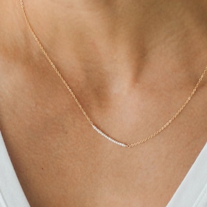 May include: A delicate gold chain necklace with a small row of white gemstones in the center.