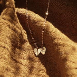 May include: A gold chain necklace with two heart-shaped pendants. The pendants have the letters "A" and "K" engraved on them.