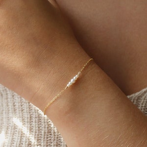 May include: A delicate gold chain bracelet with three small white pearls.