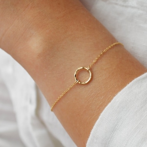 May include: A delicate gold chain bracelet with a simple circle pendant. The chain is thin and delicate, and the circle is smooth and polished.